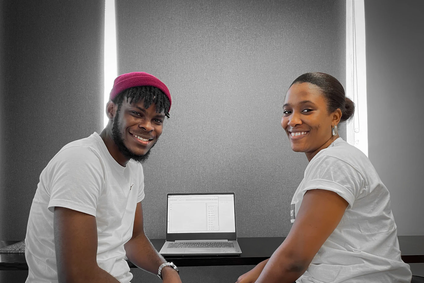 Two colleagues smiling at their desk beside a laptop